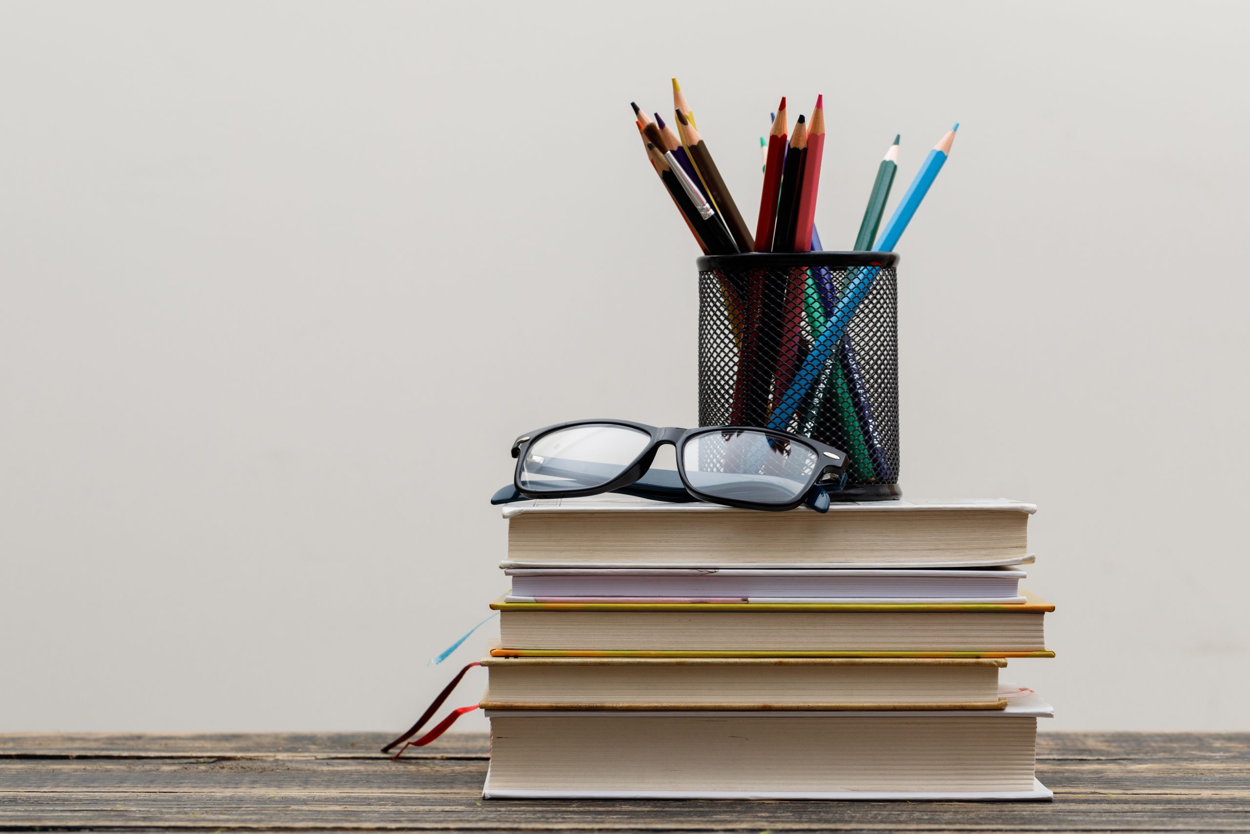 Back to school concept with glasses, books, pencils in holder on wooden and white background side view.